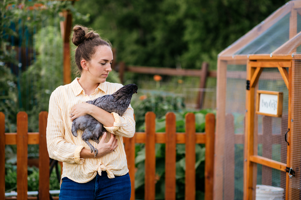 woman with pet chicken in front of coop